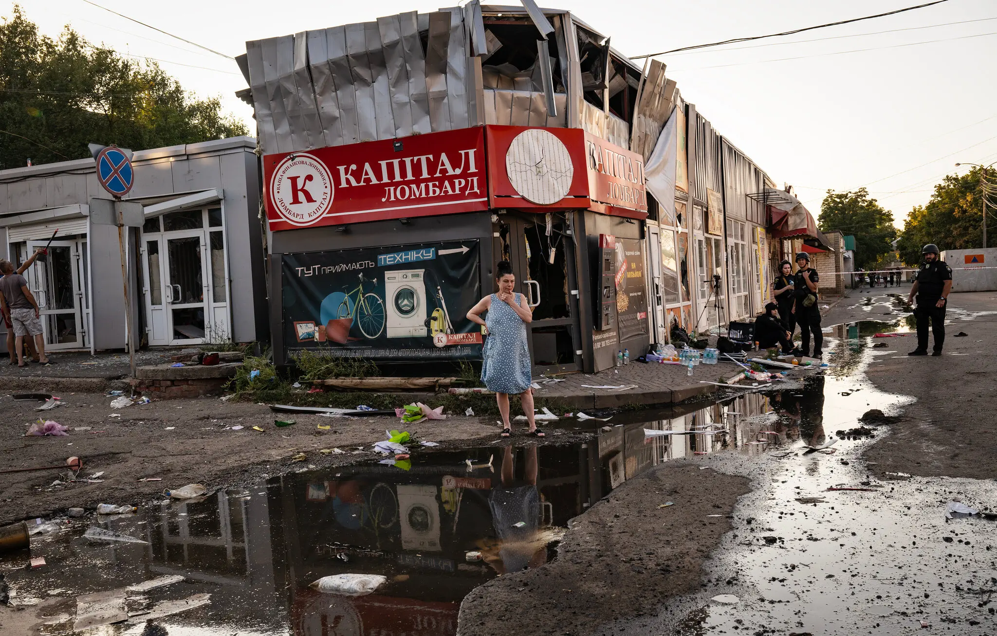 Жінка спостерігає, як українські сили безпеки досліджують місце ракетного удару, в результаті якого щонайменше 16 людей загинули та 25 отримали поранення на жвавому ринку в Костянтинівці, на сході України, 6 вересня
